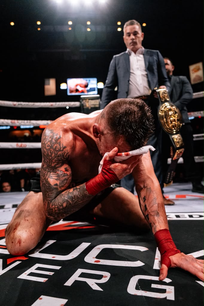Dustin Pague kneeling in the ring beside the championship belt